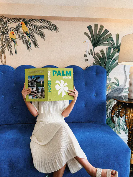 Frau liest ein Palm-Beach-Buch auf einem blauen Samtsofa