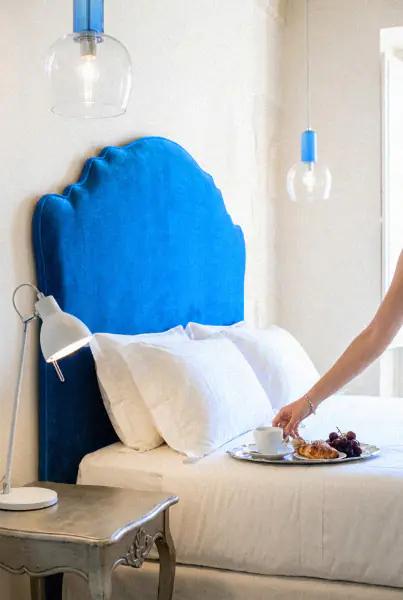 Frühstückstablett wird auf ein Bett mit blauem Samtkopfteil gestellt