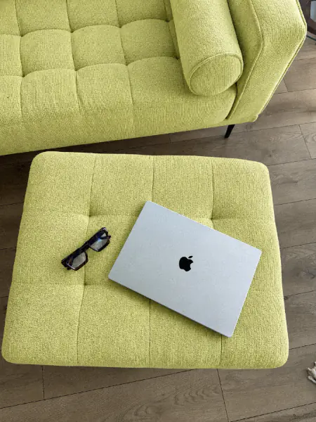Laptop und Brille auf einer hellgrünen Bouclé-Ottomane