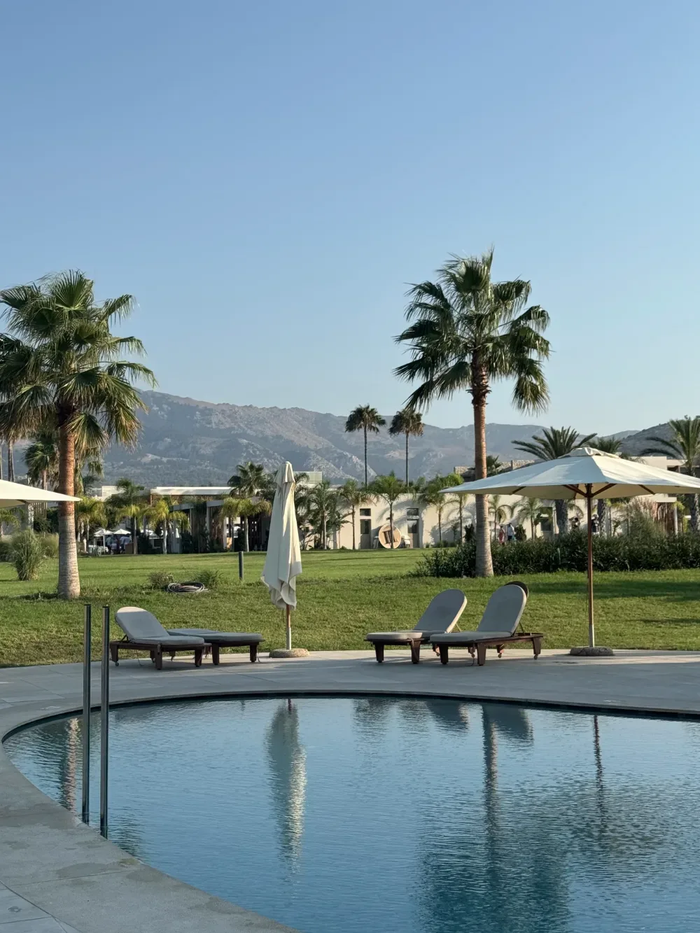 Hotelpool mit Sonnenliegen, Palmen und Bergen im Hintergrund