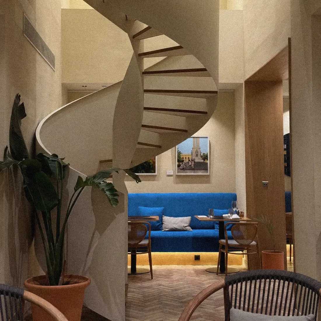 Salón de hotel con una escalera de caracol escultural y un banco corrido azul